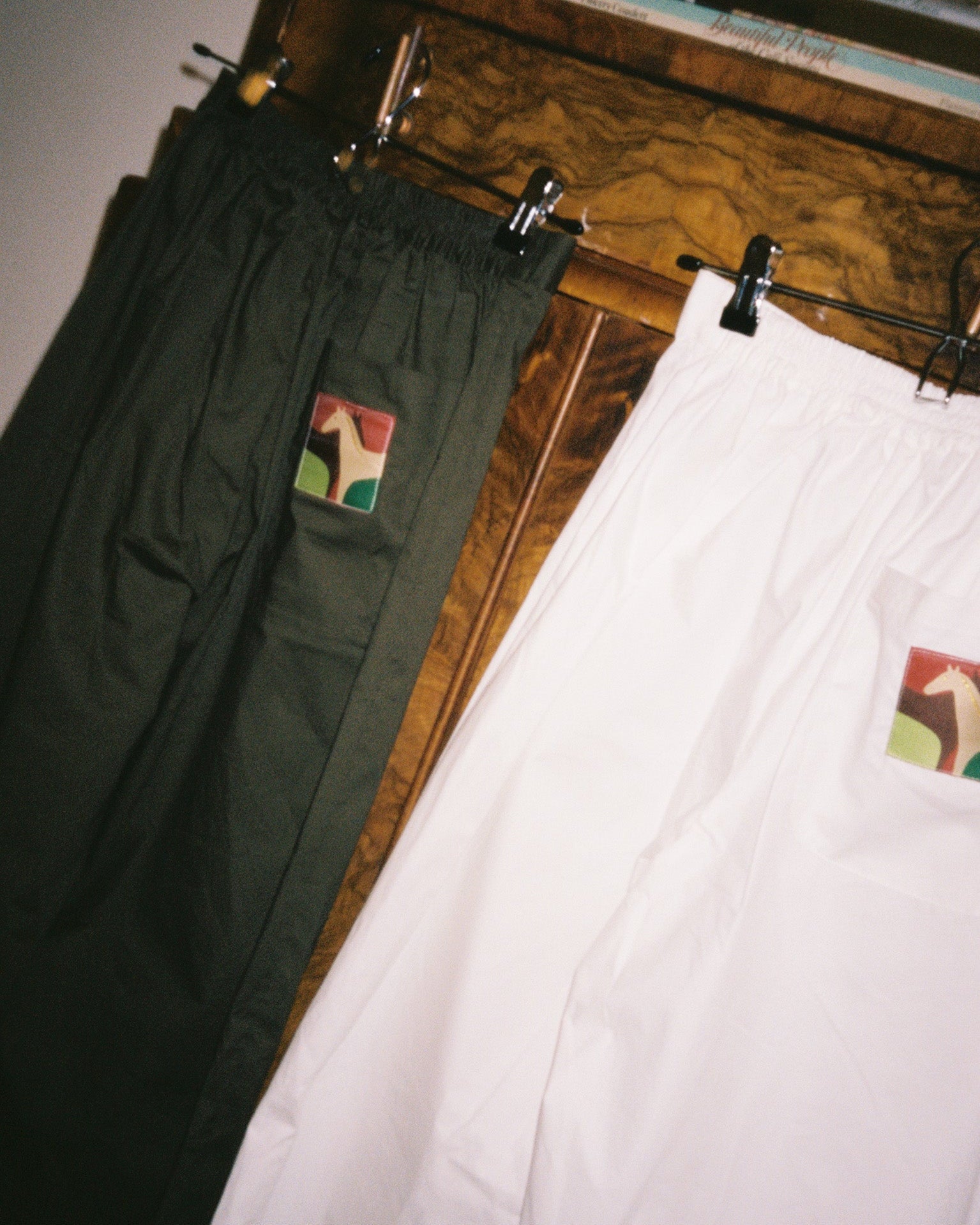 Two pairs of pants hanging on a wooden rack with a visible brand logo.